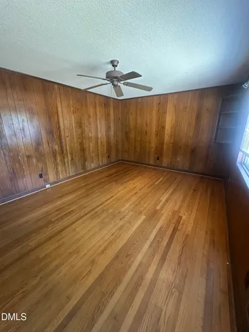 an empty room with wooden floor fan and windows