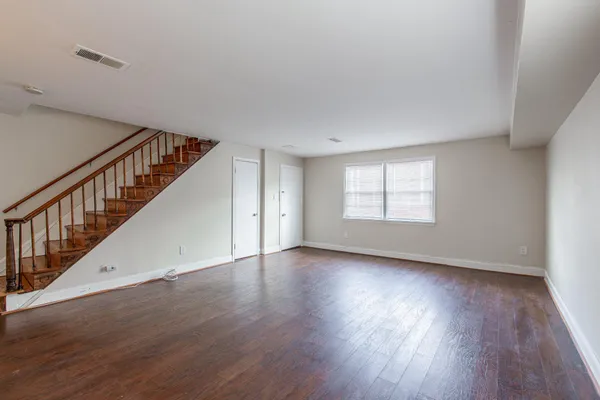a view of an empty room with wooden floor and fan
