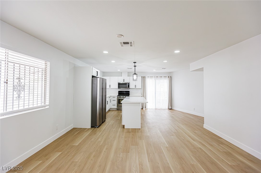 661 Riata Way Las Vegas, NV 89110 - Photo 7 of 30 Kitchen with pendant lighting, a center island, stainless steel appliances, white cabinetry, and light wood-style flooring