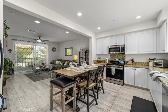 a kitchen with stainless steel appliances kitchen island granite countertop a stove a sink a refrigerator a dining table and chairs with wooden floor