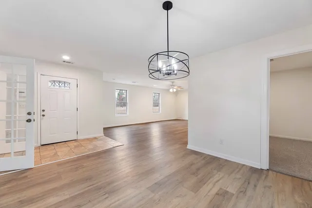 a view of an empty room with wooden floor and chandelier