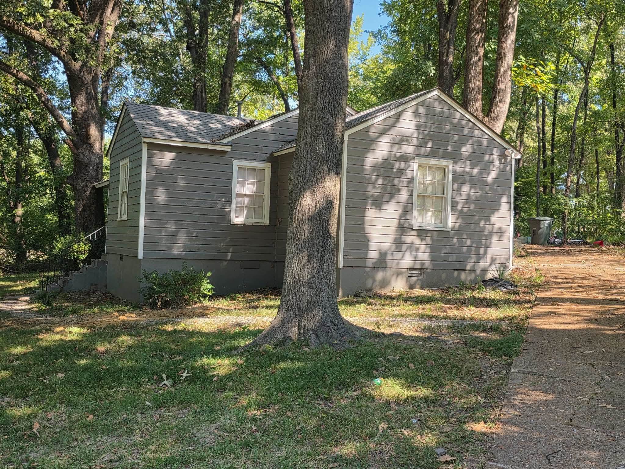 Exterior featuring grey siding, white trim windows, a sloped roof, and surrounding mature trees