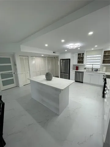 a large white kitchen with a refrigerator a stove top oven a dining table and chairs