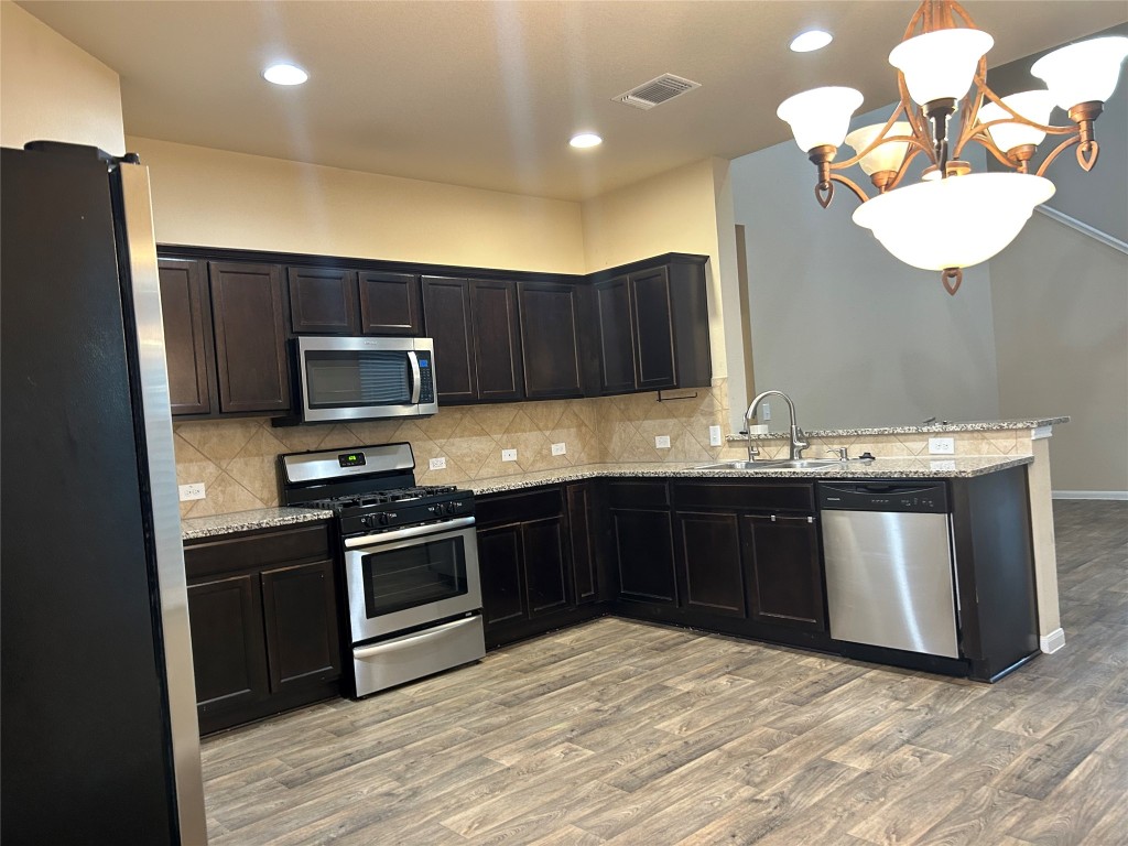 a kitchen with stainless steel appliances granite countertop a sink a stove top oven and wooden floor