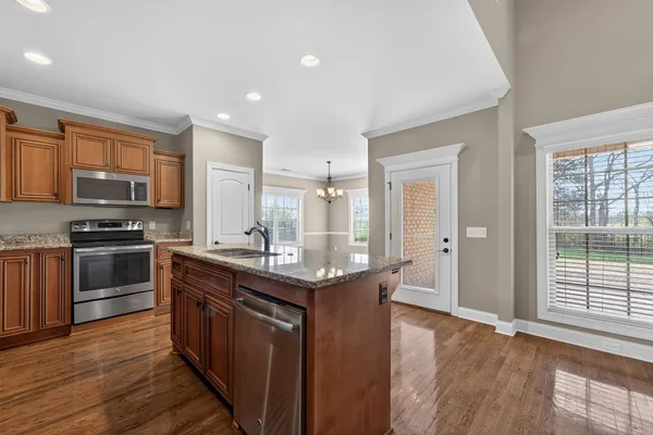 a kitchen with stainless steel appliances granite countertop a stove top oven a sink dishwasher a refrigerator and a dining table with wooden floor