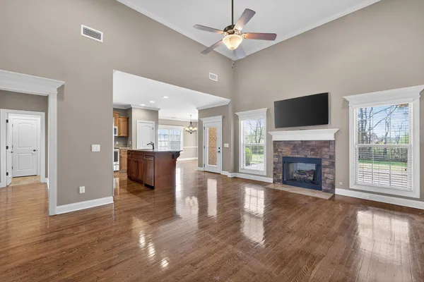 a view of a livingroom with a fireplace a ceiling fan and a kitchen view