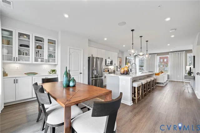 a kitchen with kitchen island a dining table chairs stainless steel appliances cabinets and wooden floor