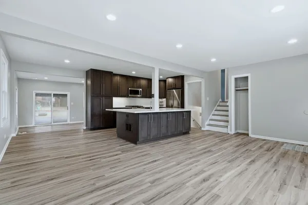 a view of kitchen with microwave oven a refrigerator and white cabinets with wooden floor