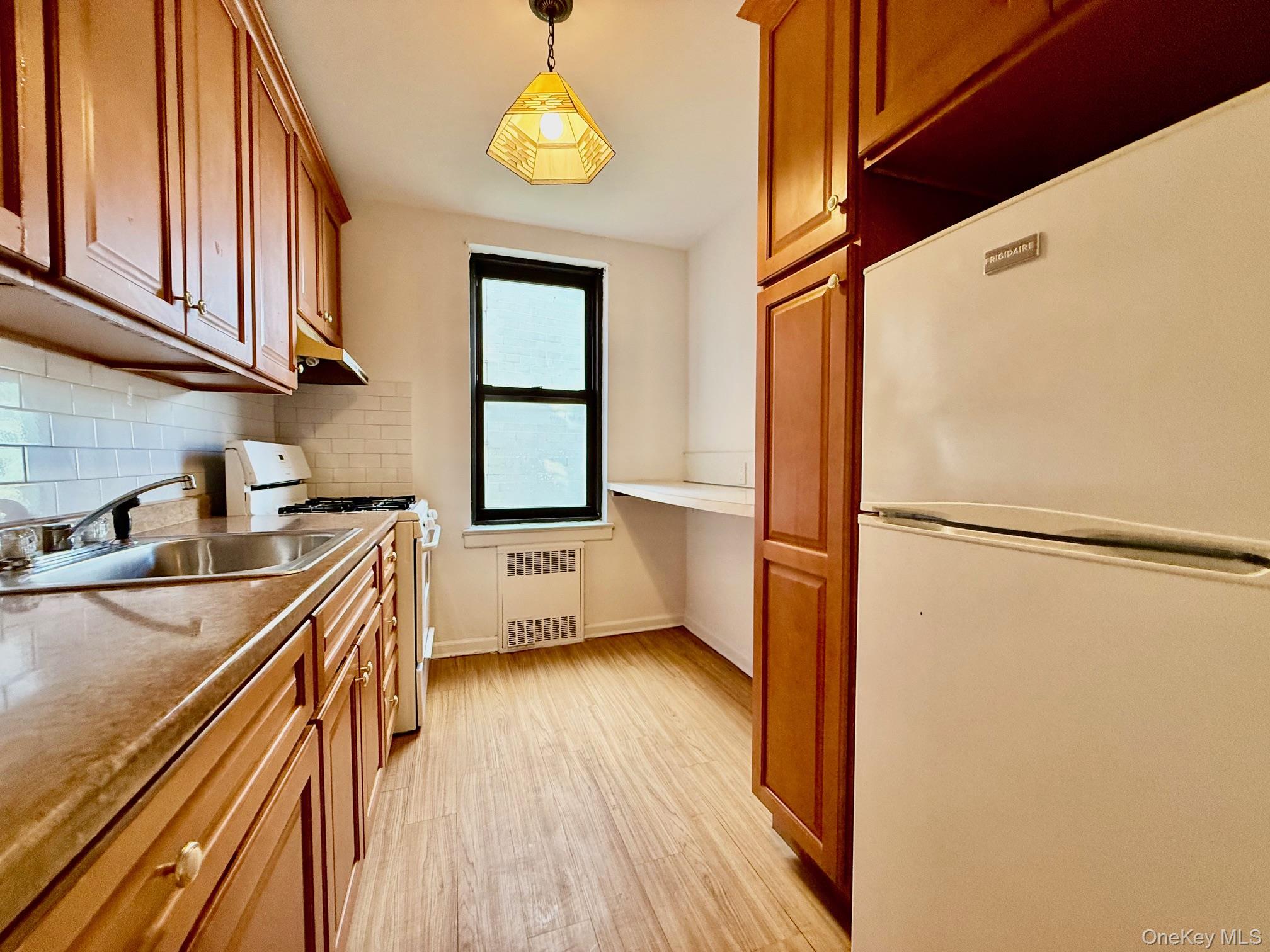 112-24 Northern Boulevard, Unit 3G Queens, NY 11368 - Photo 2 of 33 Kitchen with white appliances, light wood finished floors, brown cabinetry, and pendant lighting