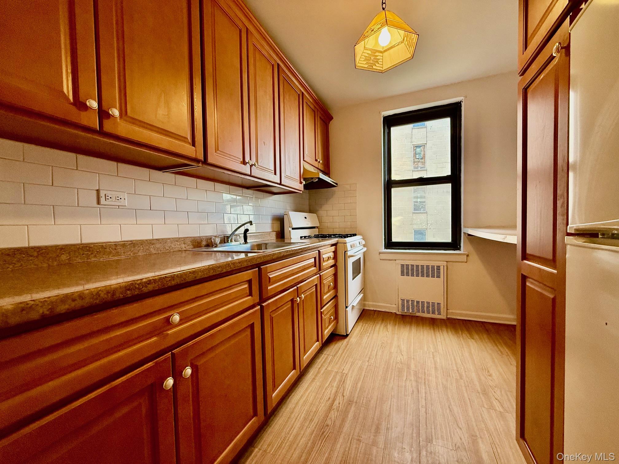 112-24 Northern Boulevard, Unit 3G Queens, NY 11368 - Photo 5 of 33 Kitchen with white appliances, tasteful backsplash, light wood-style floors, brown cabinets, and radiator