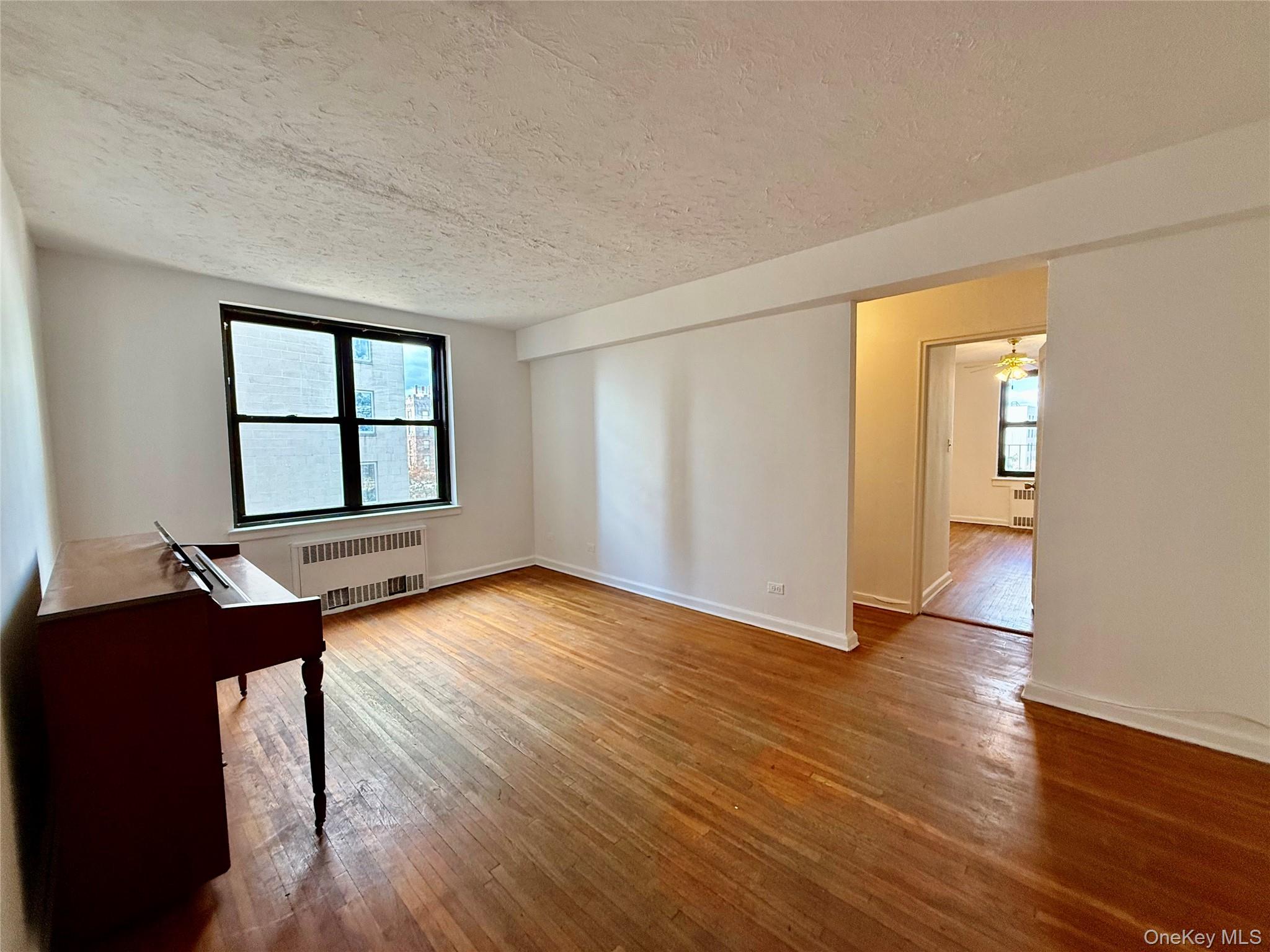 112-24 Northern Boulevard, Unit 3G Queens, NY 11368 - Photo 7 of 33 Living room featuring light wood-style floors, radiator heating unit, a textured ceiling, and ceiling fan
