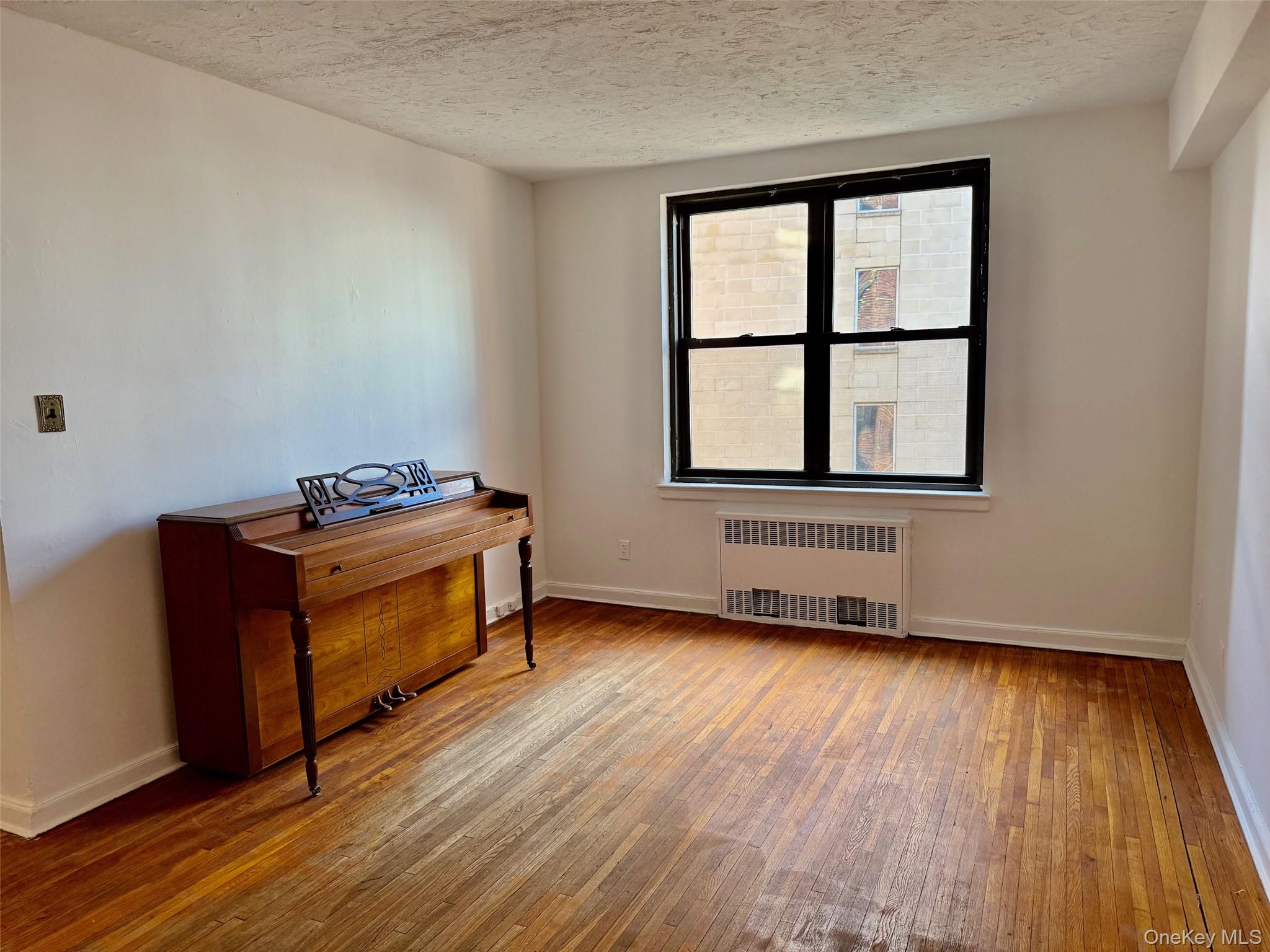 112-24 Northern Boulevard, Unit 3G Queens, NY 11368 - Photo 9 of 33 Living room with radiator heating unit, wood finished floors, and a textured ceiling