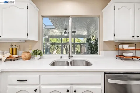 a large white kitchen with granite countertop a white stove a sink and white cabinets with wooden floor