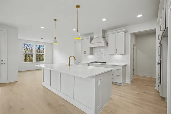 a large white kitchen with stainless steel appliances granite countertop a stove a sink a refrigerator and a dining table with wooden floor