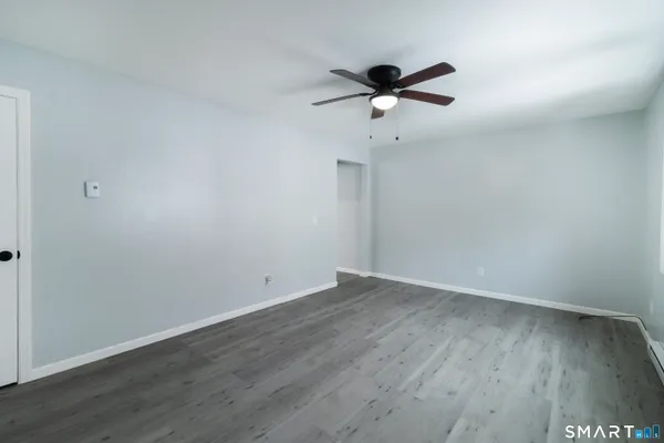 a view of an empty room with wooden floor and a ceiling fan