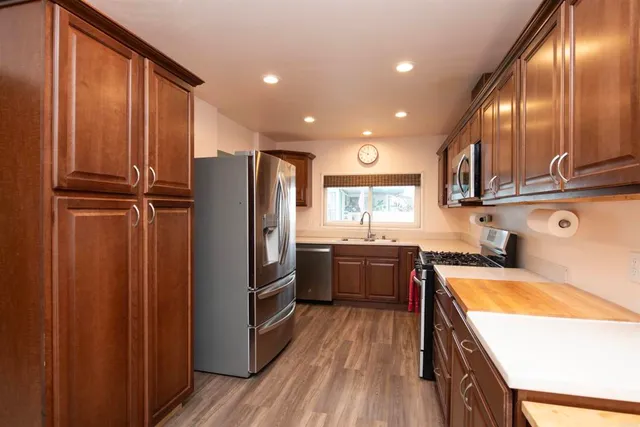 a kitchen with granite countertop stainless steel appliances a refrigerator a sink and wooden cabinets