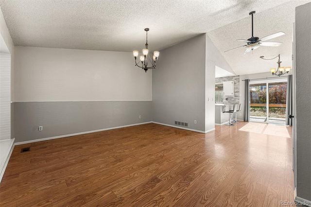 an empty room with wooden floor chandelier and windows