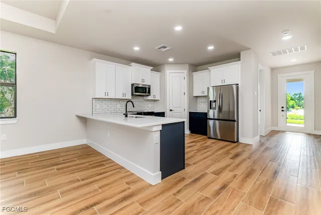 a large kitchen with kitchen island a sink dishwasher a refrigerator and a stove with wooden floor