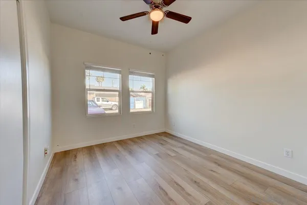an empty room with wooden floor chandelier fan and windows