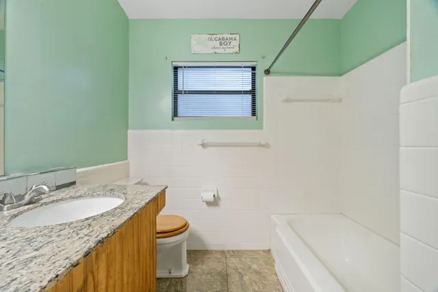 a bathroom with a granite countertop bathtub sink vanity mirror and toilet