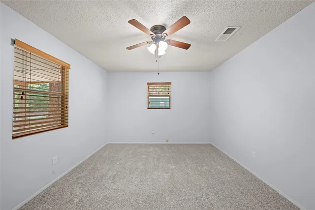 an empty room with chandelier fan and windows