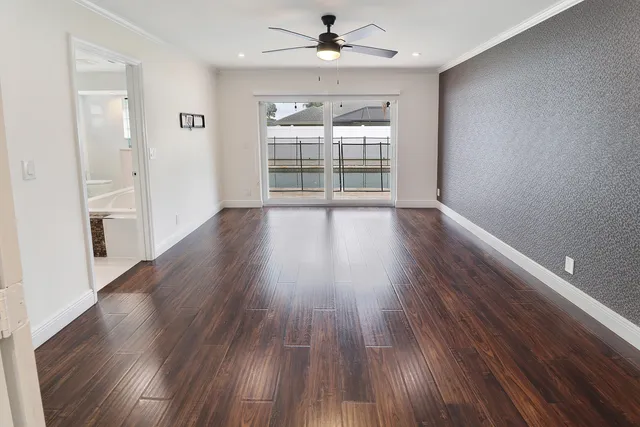 a view of an empty room with wooden floor and a ceiling fan