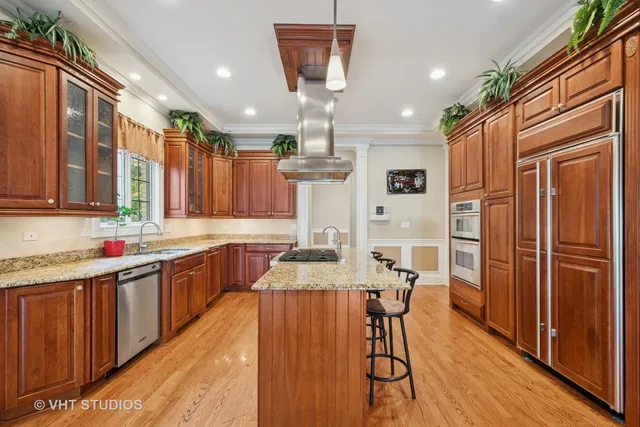 a kitchen with stainless steel appliances granite countertop a refrigerator a sink dishwasher a stove and a dining table with wooden floor