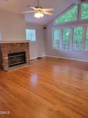 an empty room with wooden floor fireplace and windows
