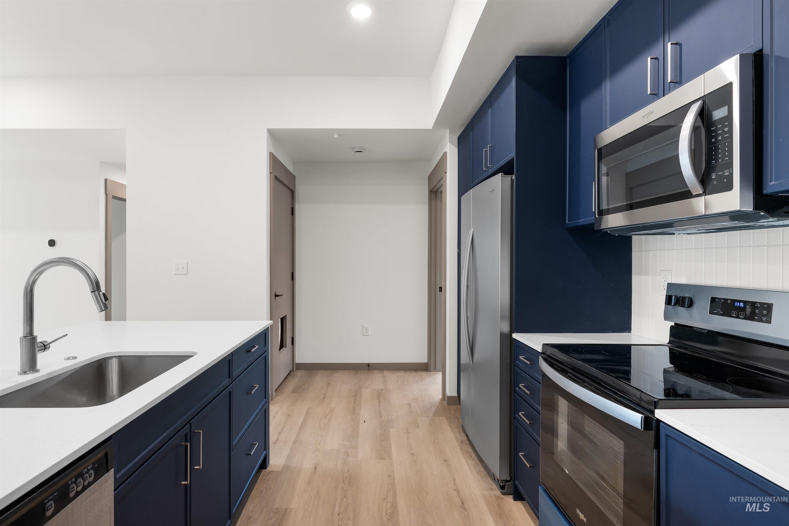 2010 Wimbledon Court Hailey, ID 83333 - Photo 5 of 46 Kitchen featuring blue cabinetry, stainless steel appliances, light wood-type flooring, light stone countertops, and tasteful backsplash