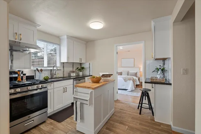 a kitchen with stainless steel appliances granite countertop a stove a sink dishwasher and white cabinets with wooden floor