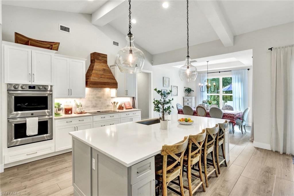 3700 11th Avenue Southwest Naples, FL 34117 - Photo 12 of 50 a kitchen with stainless steel appliances a stove a sink dishwasher a refrigerator white cabinets a dining table and chairs with wooden floor