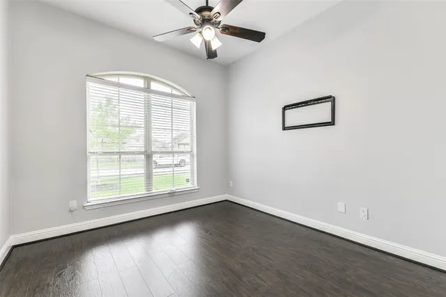 an empty room with wooden floor chandelier fan and windows