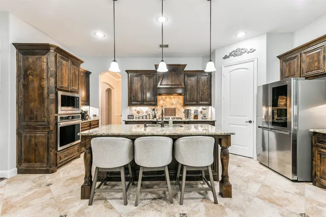 a kitchen with stainless steel appliances granite countertop a sink a stove a refrigerator and chairs