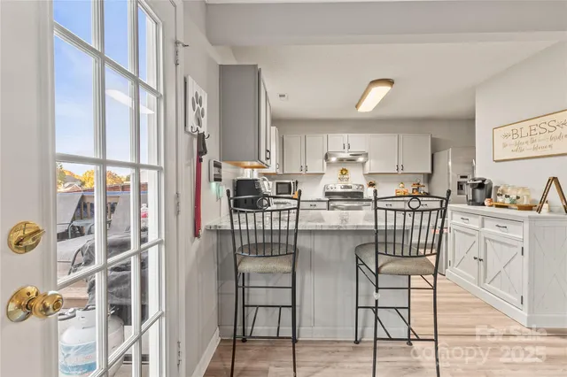 a kitchen with stainless steel appliances kitchen island granite countertop a refrigerator a stove a dining table and chairs with wooden floor