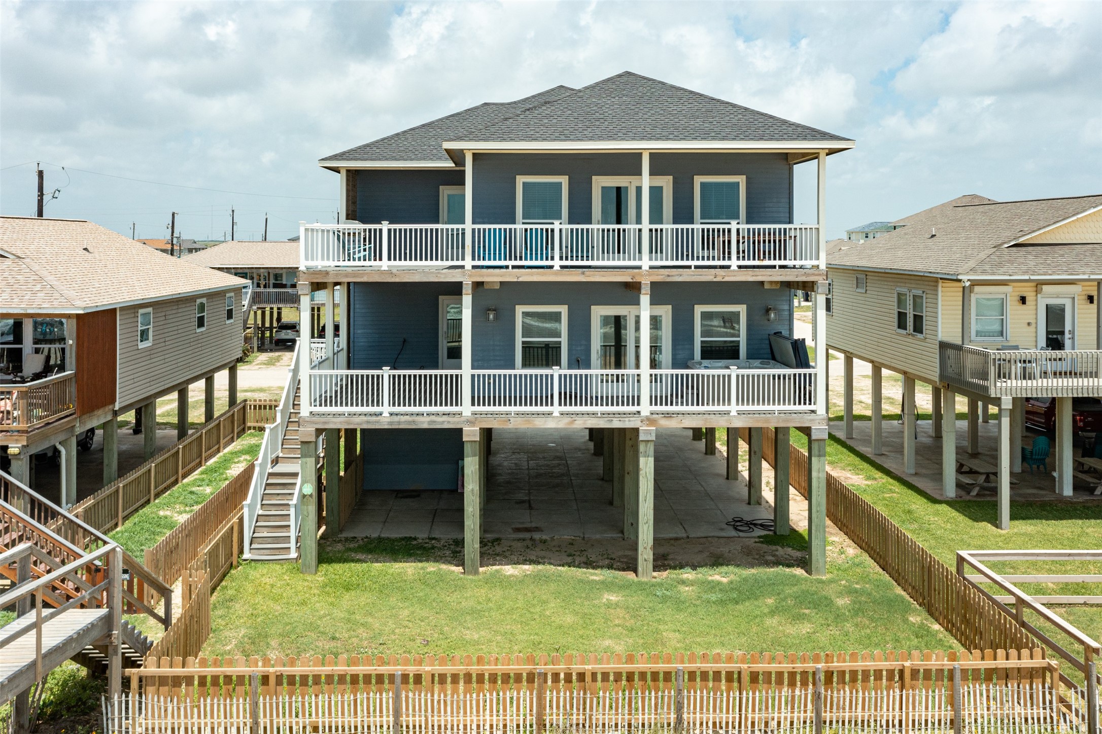 109 A Santar Loop, Unit A Surfside Beach, TX 77541 - Photo 1 of 43 Elevated two-story home with a modern design, featuring spacious balconies on both levels. The property includes a fenced yard and an open area beneath the house, ideal for parking or storage. Located in a coastal neighborhood with other similar elevated homes.