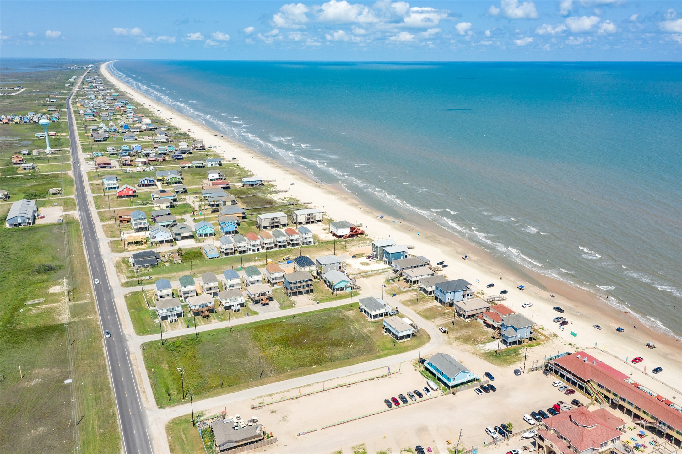 109 A Santar Loop, Unit A Surfside Beach, TX 77541 - Photo 12 of 43 This aerial photo showcases a coastal residential area with numerous homes lining a long stretch of sandy beach. The ocean view is expansive, and the neighborhood is accessible by a main road. Ideal for buyers seeking a beachside lifestyle.
