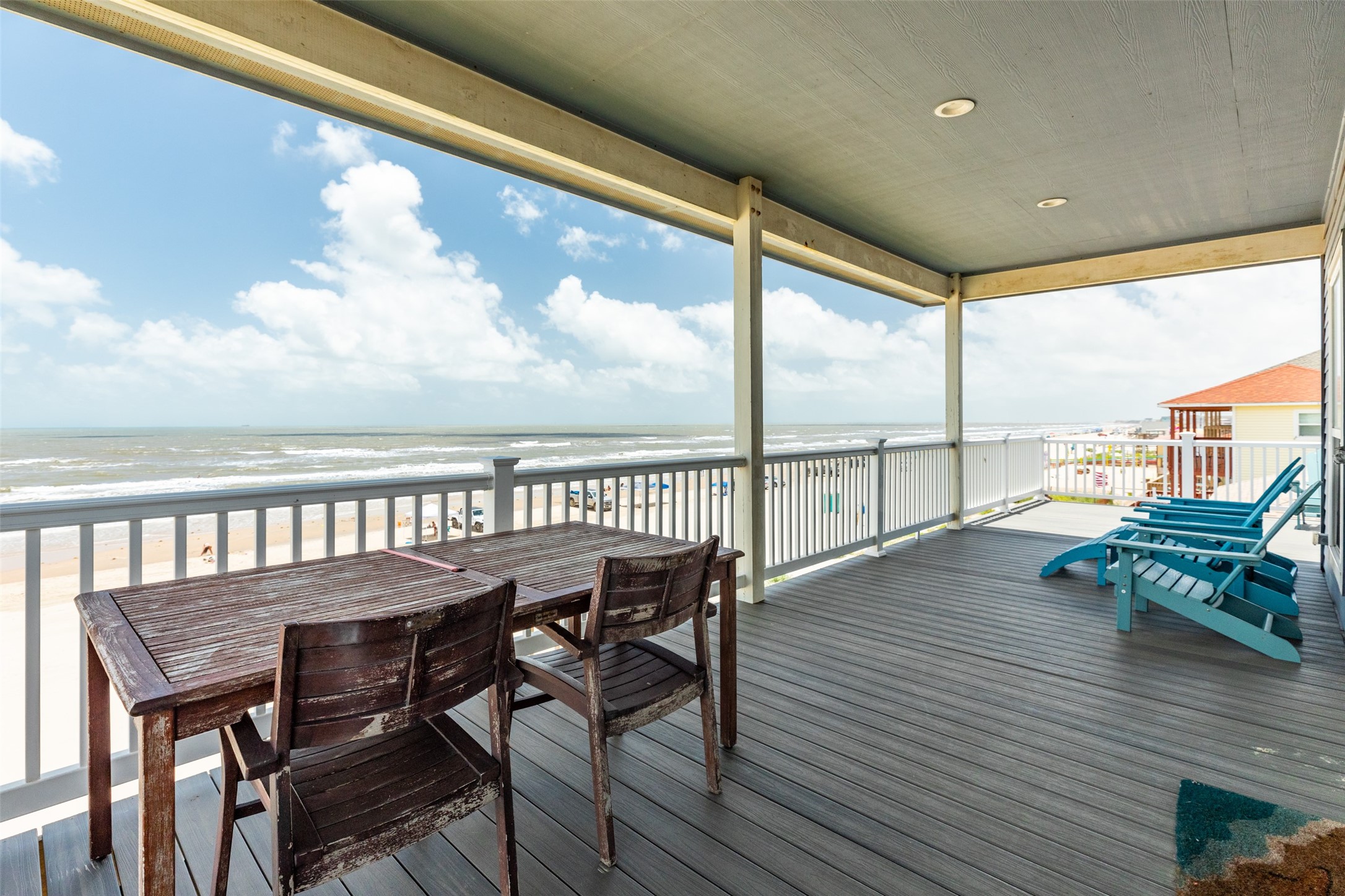 109 A Santar Loop, Unit A Surfside Beach, TX 77541 - Photo 20 of 43 Spacious beachfront deck with stunning ocean views, featuring wooden dining furniture and vibrant blue lounge chairs, perfect for relaxing and entertaining.