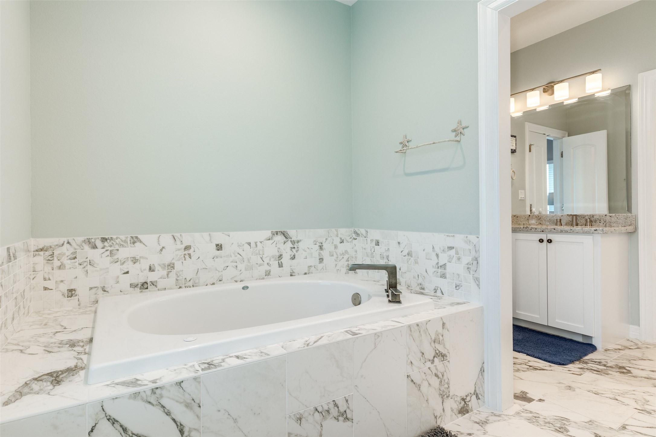 109 A Santar Loop, Unit A Surfside Beach, TX 77541 - Photo 28 of 43 This bathroom features a luxurious marble-look tiled bathtub, soft pastel walls, and a modern sink area with a large mirror and ample lighting.