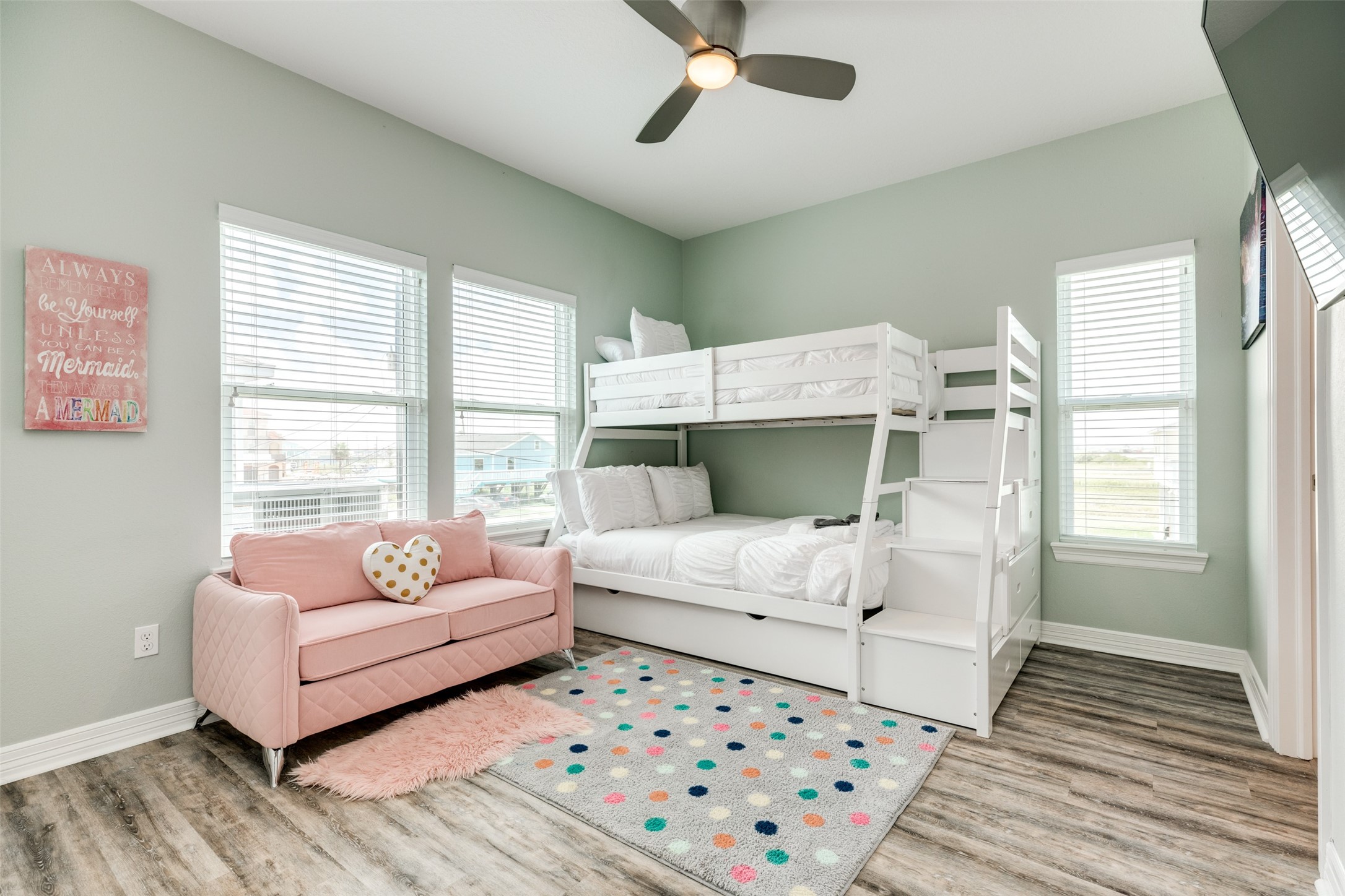109 A Santar Loop, Unit A Surfside Beach, TX 77541 - Photo 29 of 43 This bright and inviting bedroom features a cozy bunk bed with stairs, a pink sofa with a heart pillow, and stylish wood flooring. Large windows provide ample natural light, and the room is decorated with cheerful accents. Perfect for a extra space.