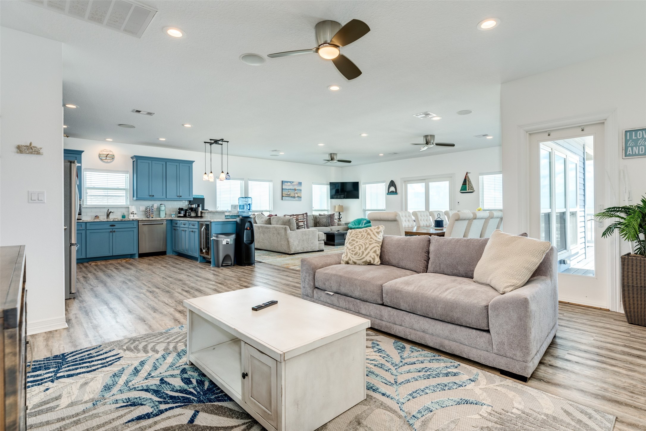 109 A Santar Loop, Unit A Surfside Beach, TX 77541 - Photo 33 of 43 Spacious open-concept living area with modern kitchen featuring blue cabinetry, stainless steel appliances, and ample natural light. The room includes cozy seating, a stylish rug, and ceiling fans, offering a welcoming and functional space for gatherings.