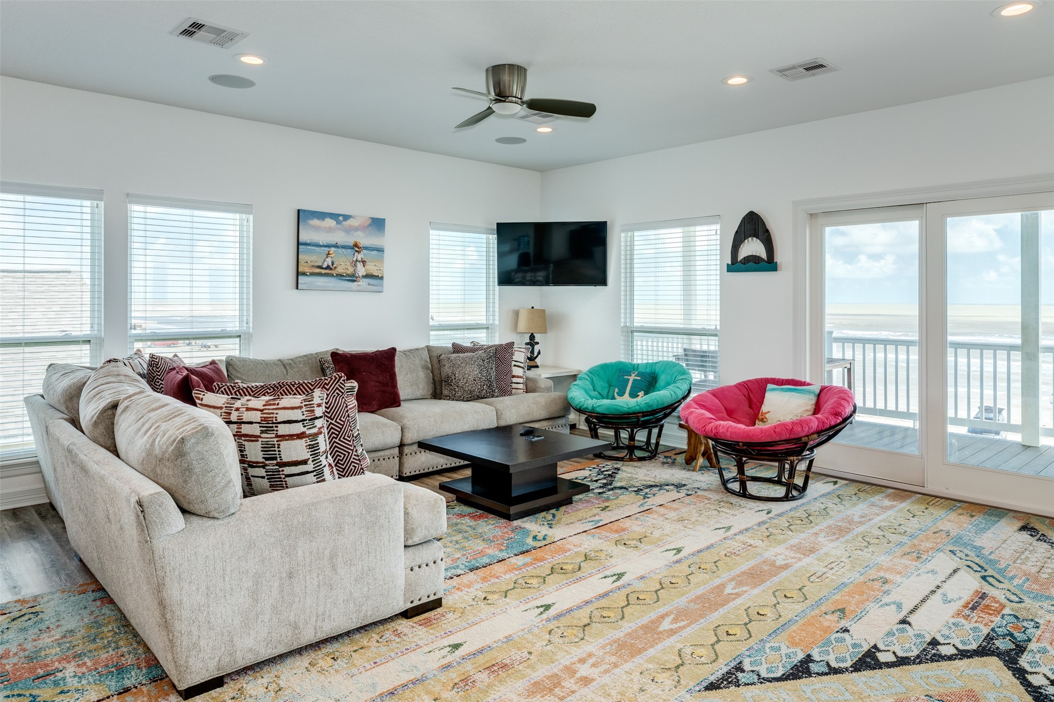 109 A Santar Loop, Unit A Surfside Beach, TX 77541 - Photo 37 of 43 Bright and inviting living room with large windows offering ocean views. Features a cozy sectional sofa, colorful accent chairs, and a ceiling fan. A glass door leads to a spacious deck.