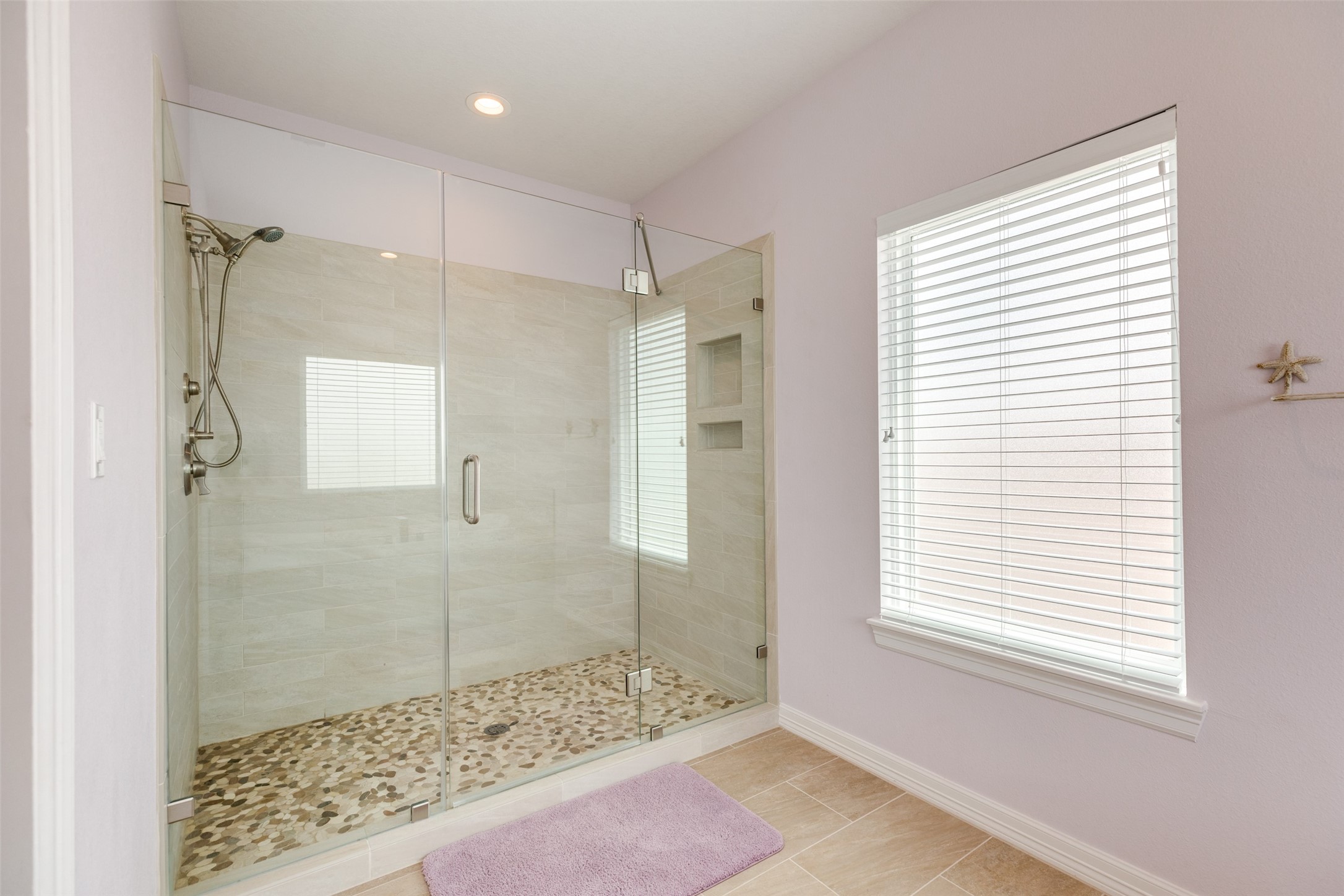 109 A Santar Loop, Unit A Surfside Beach, TX 77541 - Photo 41 of 43 Modern bathroom featuring a spacious glass-enclosed shower with stylish tile work and pebble flooring. The room is brightened by a large window with blinds, adding a touch of elegance and privacy.