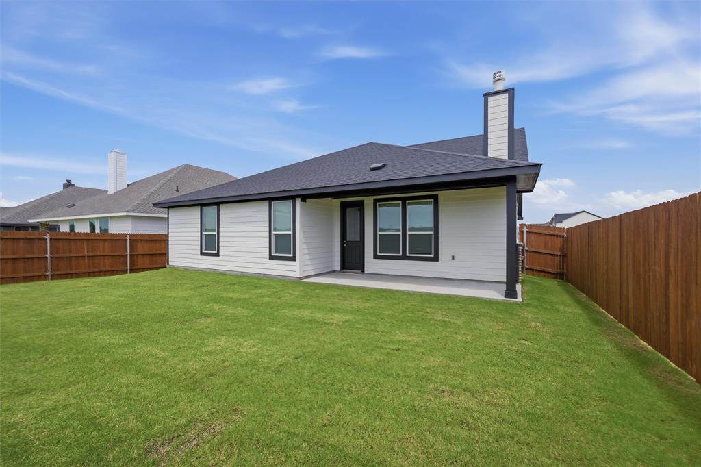 1325 Frio Drive Springtown, TX 76082 - Photo 21 of 24 Spacious backyard with a substantial lawn area, featuring a covered patio, dark framed windows, and a privacy fence