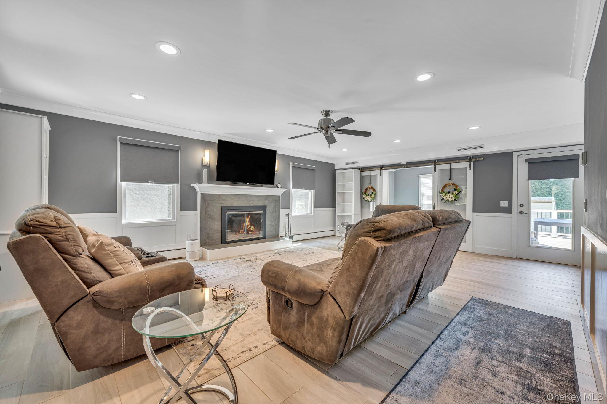 183 Old Country Road Speonk, NY 11972 - Photo 21 of 48 Living room featuring wainscoting, a decorative wall, a barn door, ceiling fan, and light wood-style flooring