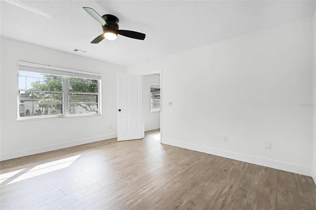an empty room with wooden floor chandelier fan and windows