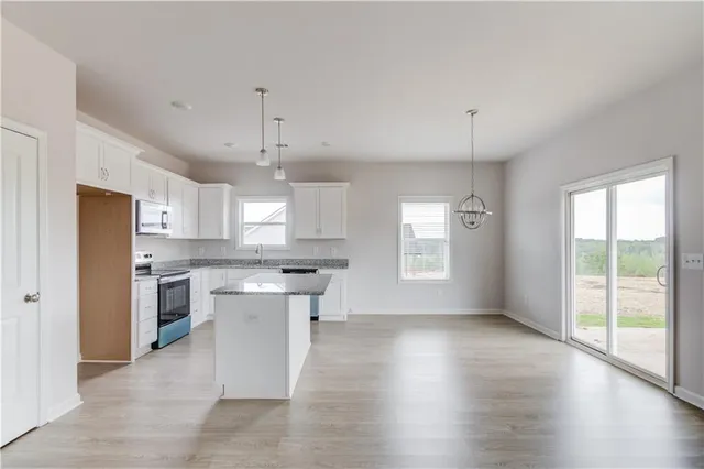 a kitchen with stainless steel appliances granite countertop a stove a sink dishwasher a refrigerator white cabinets and wooden floor next to a window