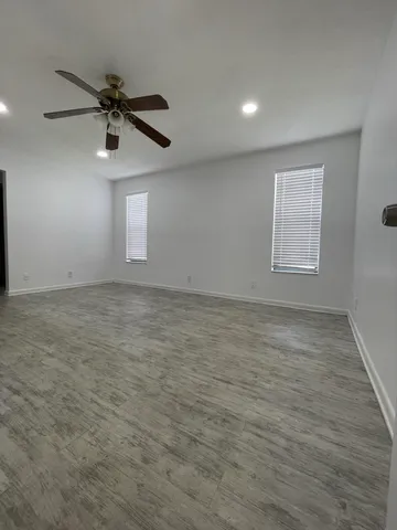 an empty room with wooden floor ceiling fan and windows