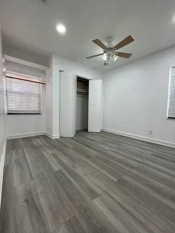 an empty room with wooden floor fan and windows