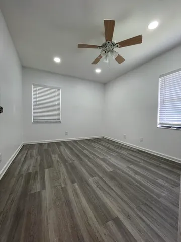 an empty room with wooden floor chandelier fan and windows