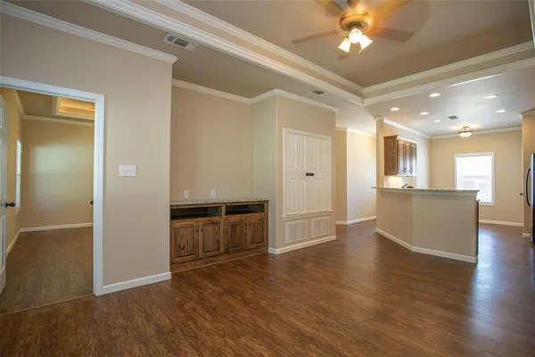 a view of an empty room and kitchen with wooden floor